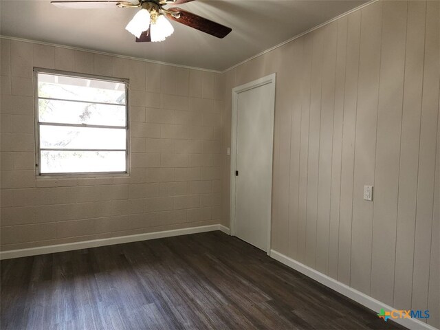 unfurnished room with ornamental molding, dark wood finished floors, a ceiling fan, and baseboards