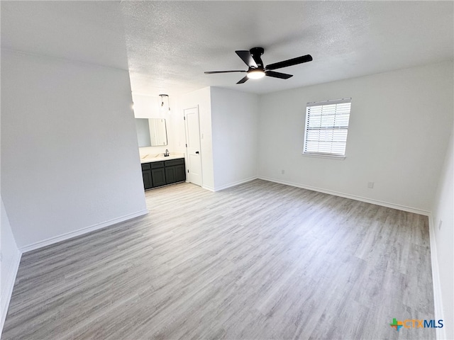 unfurnished living room featuring sink, a textured ceiling, ceiling fan, and light hardwood / wood-style flooring