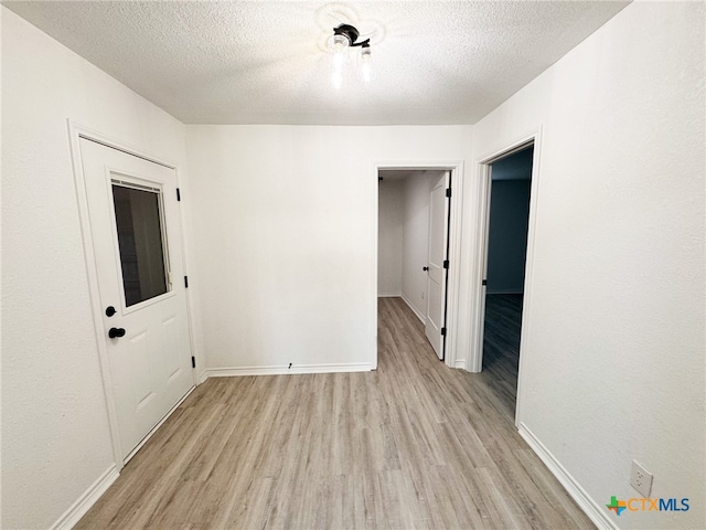 unfurnished room with a textured ceiling and light wood-type flooring