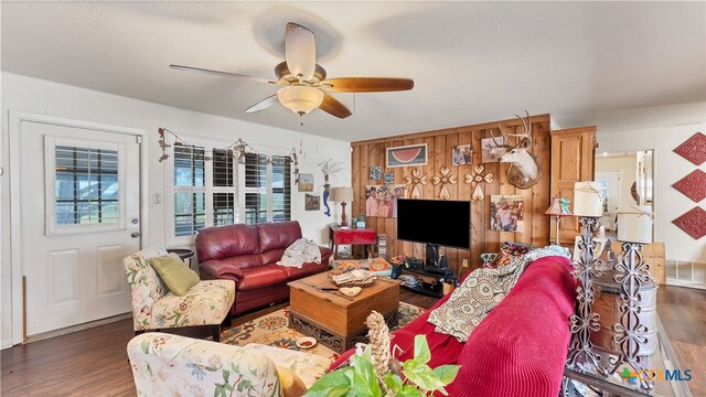 living room featuring ceiling fan, dark hardwood / wood-style floors, and wood walls