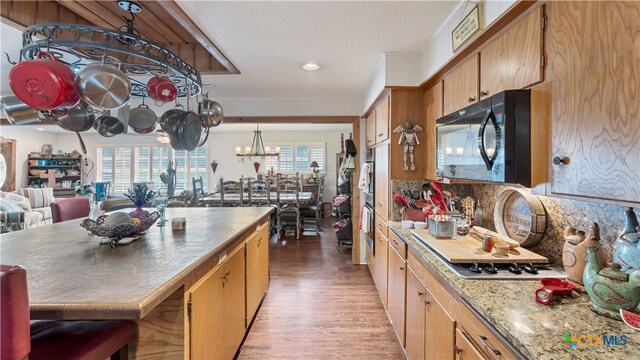 kitchen with stainless steel gas cooktop, light wood-type flooring, backsplash, hanging light fixtures, and a chandelier