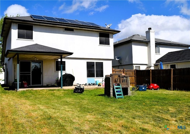 back of house with fence, a lawn, stucco siding, and solar panels