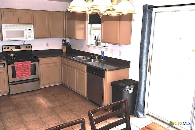 kitchen with dark countertops, a sink, dark tile patterned floors, a chandelier, and appliances with stainless steel finishes
