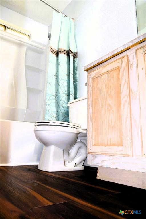 interior details featuring wood finished floors, toilet, and a shower with curtain