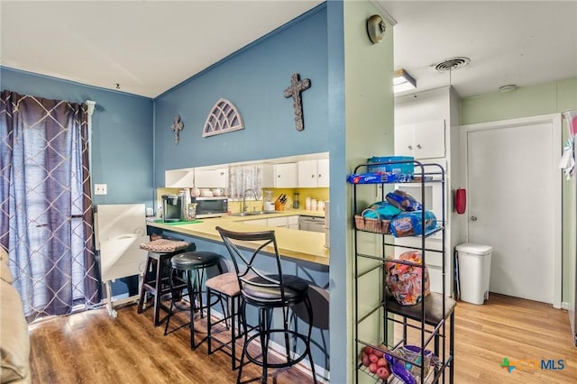 kitchen featuring sink, light hardwood / wood-style flooring, white cabinetry, a kitchen breakfast bar, and kitchen peninsula