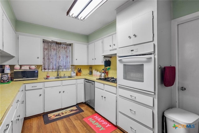 kitchen with sink, white cabinetry, backsplash, stainless steel appliances, and light wood-type flooring