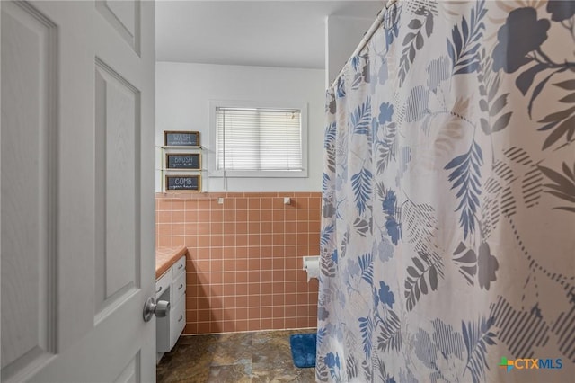 bathroom with walk in shower, vanity, and tile walls