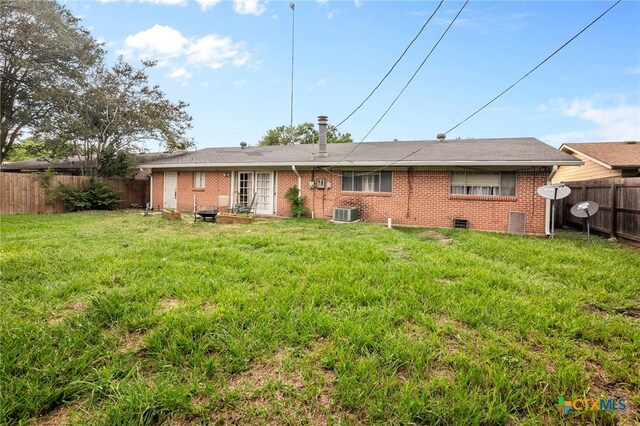 rear view of house with central air condition unit and a lawn