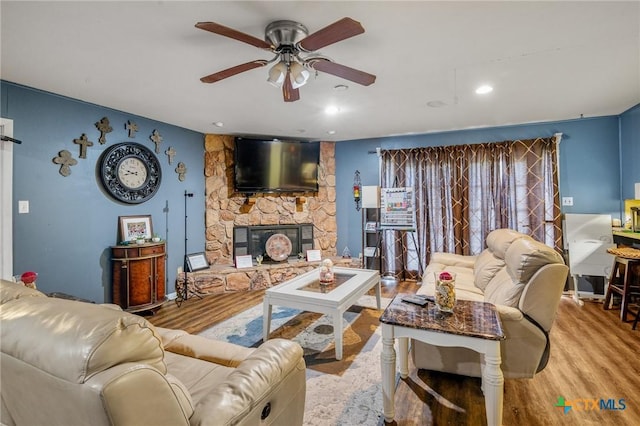 living room featuring a fireplace, ceiling fan, and light wood-type flooring