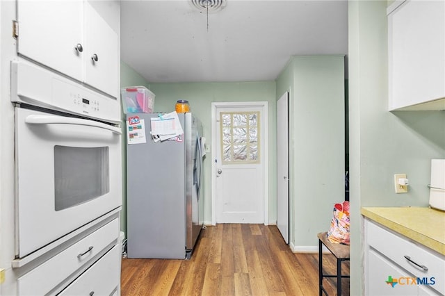 kitchen with white cabinets, stainless steel fridge, oven, and light hardwood / wood-style floors