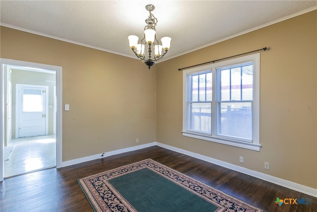 spare room with dark wood-type flooring, a wealth of natural light, a chandelier, and ornamental molding