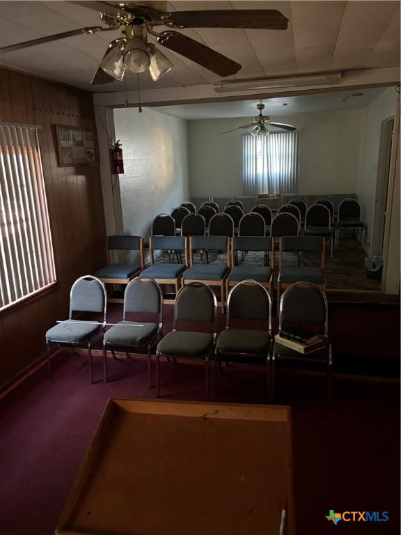 carpeted cinema featuring ceiling fan and wood walls