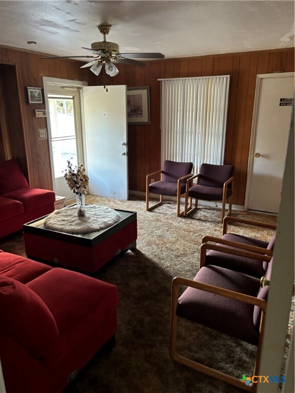 carpeted living room with ceiling fan and wood walls