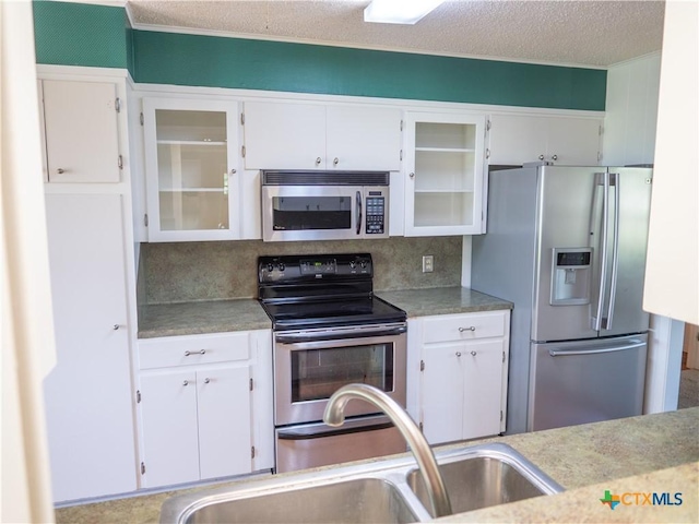 kitchen featuring glass insert cabinets, white cabinetry, a sink, and appliances with stainless steel finishes