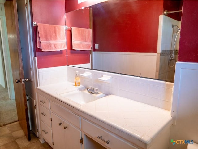 full bathroom with vanity, a tile shower, and a wainscoted wall