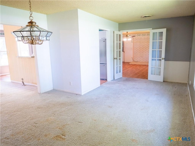 unfurnished room with a notable chandelier, french doors, a textured ceiling, and carpet floors