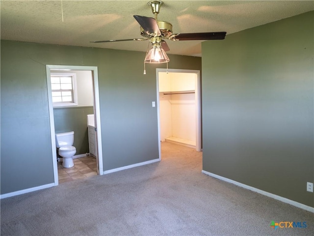 unfurnished bedroom with a walk in closet, carpet flooring, ensuite bathroom, and baseboards