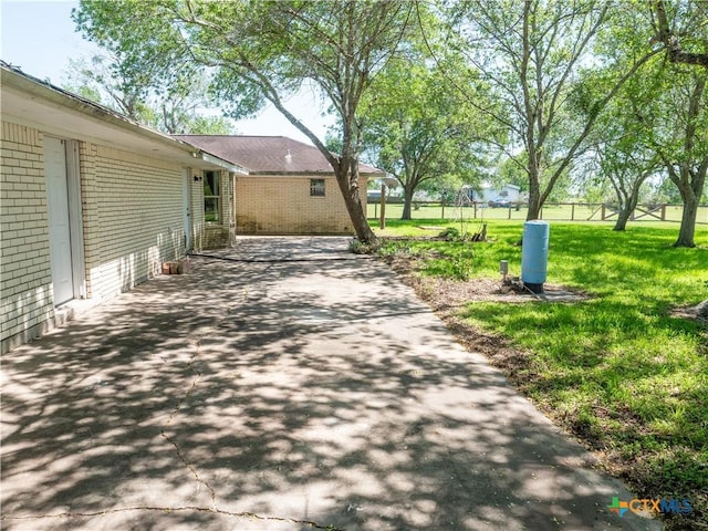 view of side of home featuring a patio area, fence, a lawn, and aphalt driveway