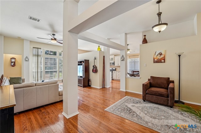 living area featuring light wood finished floors, visible vents, baseboards, and ceiling fan