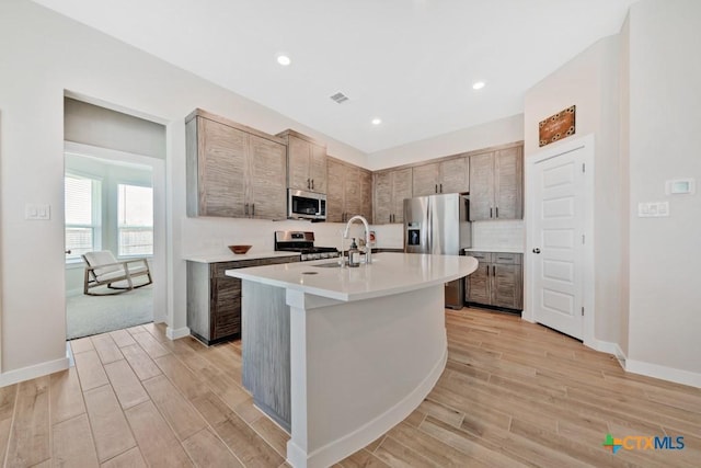 123 Paul Pena Dr, San Marcos, TX 78666 - kitchen featuring appliances with stainless steel finishes, a sink, light countertops, light wood-style floors, and a kitchen island with sink