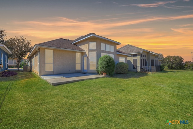 back house at dusk featuring a patio, a yard, and cooling unit