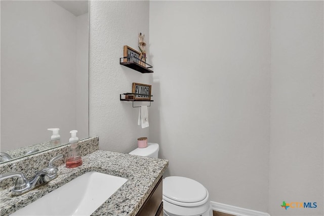 half bath with toilet, vanity, and baseboards