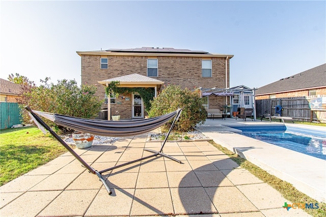 back of property with solar panels, a fenced in pool, and a patio area