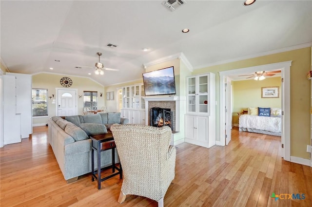 living room featuring lofted ceiling, light wood-style flooring, visible vents, and a warm lit fireplace