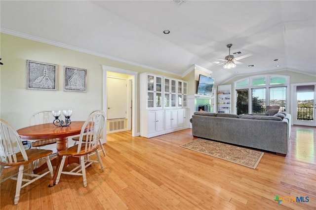 living area featuring visible vents, lofted ceiling, ornamental molding, light wood-style flooring, and a warm lit fireplace