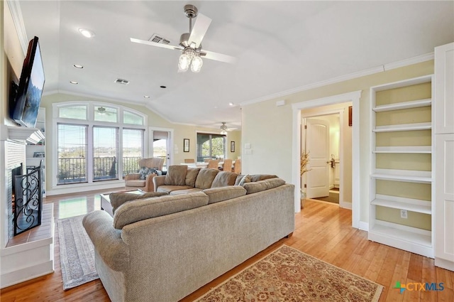 living room featuring visible vents, built in shelves, a warm lit fireplace, light wood finished floors, and vaulted ceiling