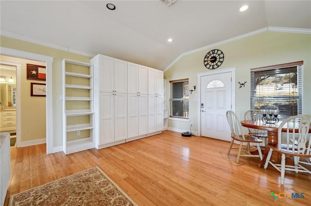 foyer with lofted ceiling, light wood-style floors, baseboards, and ornamental molding