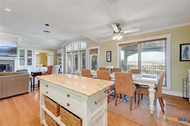 kitchen with visible vents, crown molding, lofted ceiling, light wood-style flooring, and a warm lit fireplace