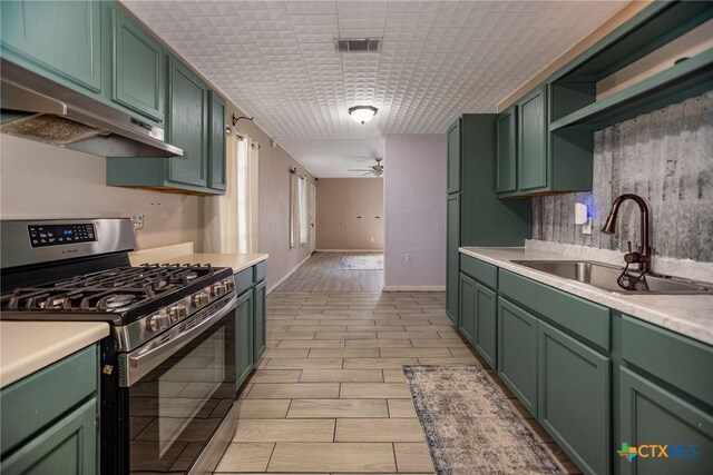 2102 Leon Dr, Port Lavaca, TX 77979 - kitchen with stainless steel gas range, green cabinetry, under cabinet range hood, ceiling fan, and light countertops