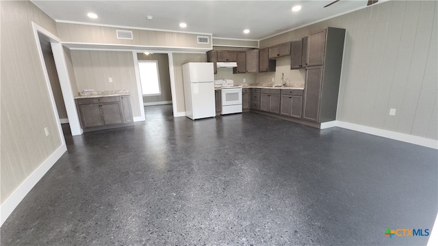 kitchen with wood walls, white appliances, sink, and dark brown cabinetry