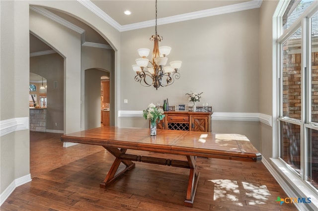 dining area featuring wood finished floors, arched walkways, a notable chandelier, and ornamental molding