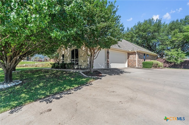 obstructed view of property featuring aphalt driveway, brick siding, a front yard, and a garage