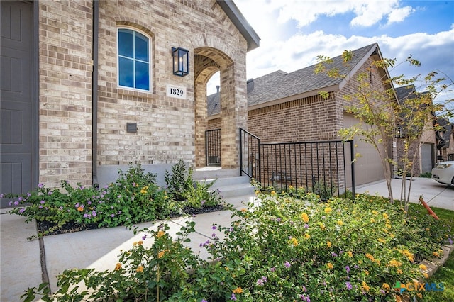 25039 Arrow Gln, San Antonio, TX 78258 - view of exterior entry featuring brick siding, a garage, driveway, and a shingled roof