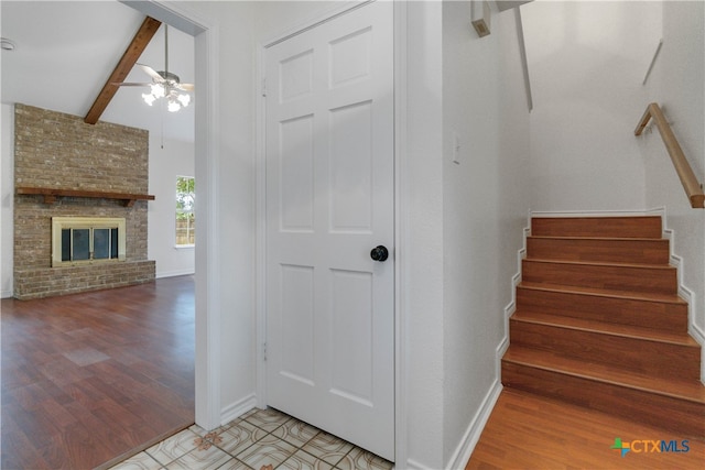 staircase with lofted ceiling with beams, hardwood / wood-style flooring, ceiling fan, and a fireplace