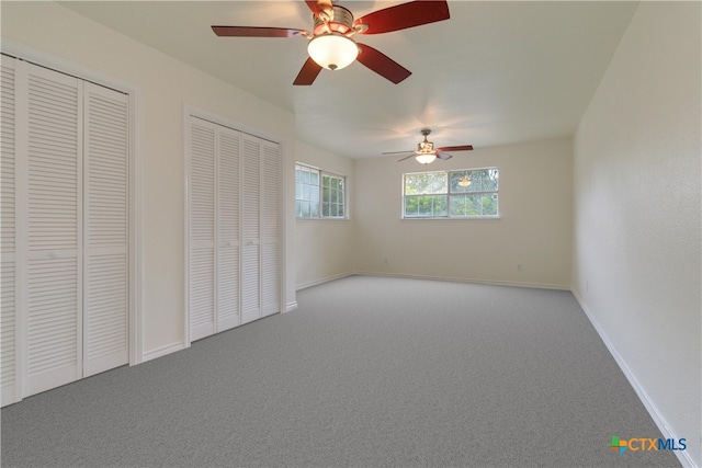 unfurnished bedroom with light carpet, ceiling fan, and two closets