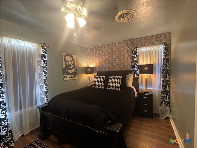 bedroom with visible vents, baseboards, wood finished floors, a textured ceiling, and a ceiling fan