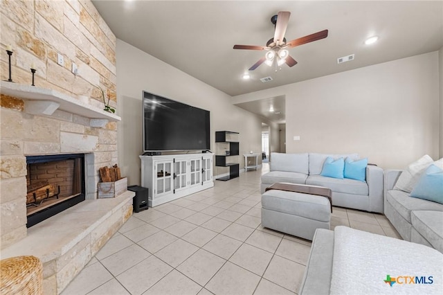 living area featuring a ceiling fan, a stone fireplace, visible vents, and light tile patterned floors