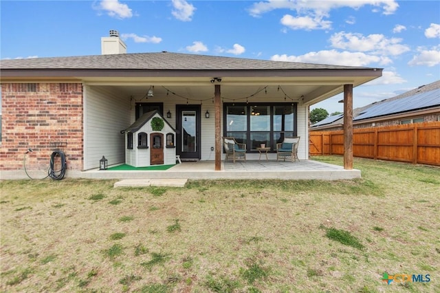 back of property featuring a chimney, a fenced backyard, a patio area, a lawn, and brick siding