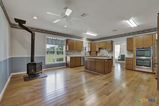 82 Bell Mountain Rd, Fredericksburg, TX 78675 - kitchen with wallpapered walls, stainless steel appliances, a wood stove, brown cabinets, and light countertops