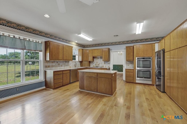 82 Bell Mountain Rd, Fredericksburg, TX 78675 - kitchen with appliances with stainless steel finishes, brown cabinetry, wallpapered walls, a kitchen island, and light wood finished floors