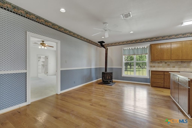 82 Bell Mountain Rd, Fredericksburg, TX 78675 - unfurnished dining area featuring wallpapered walls, ceiling fan, light wood-style floors, a wood stove, and baseboards
