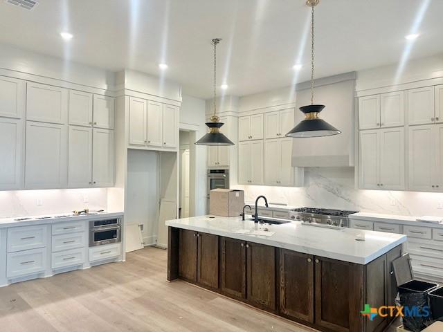 kitchen with tasteful backsplash, range, light wood-type flooring, white cabinetry, and a sink