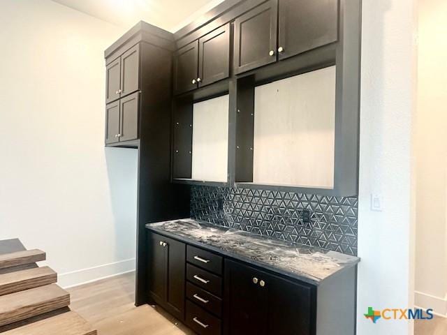 kitchen featuring tasteful backsplash, dark stone counters, baseboards, and light wood-type flooring