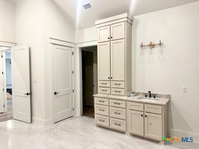 bathroom featuring vanity, visible vents, baseboards, and vaulted ceiling