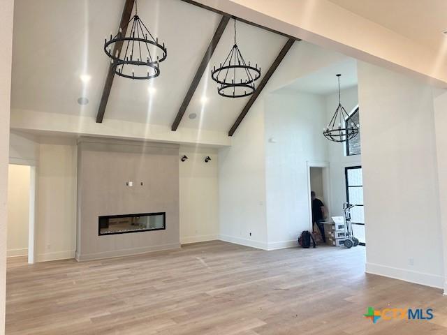 unfurnished living room featuring an inviting chandelier, a high ceiling, light wood finished floors, baseboards, and beam ceiling