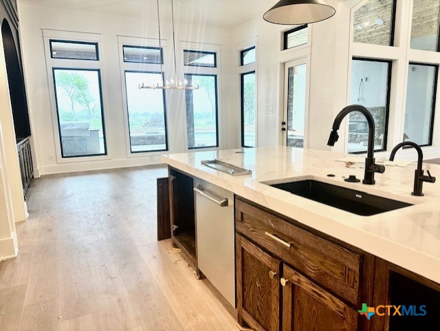 kitchen with a sink, light wood finished floors, a chandelier, and a healthy amount of sunlight